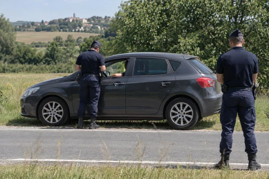 Contrôle routier : une voiture arrêtée sur le bas-côté, un agent en uniforme bleu marine près de la portière du conducteur et un second agent en retrait.